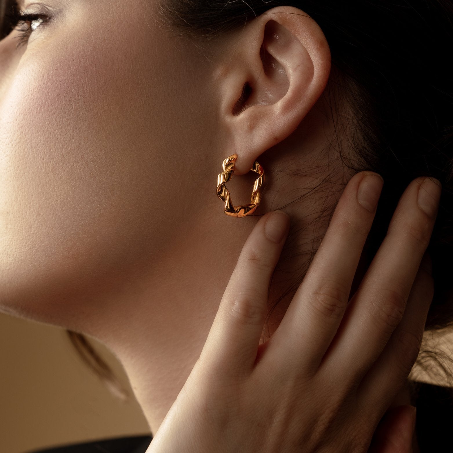 Aega Earrings Collection Earring Gold Hoops twisted Hoops girl with hand up elegantly near ear showing off her gold hoop earrings on her left ear