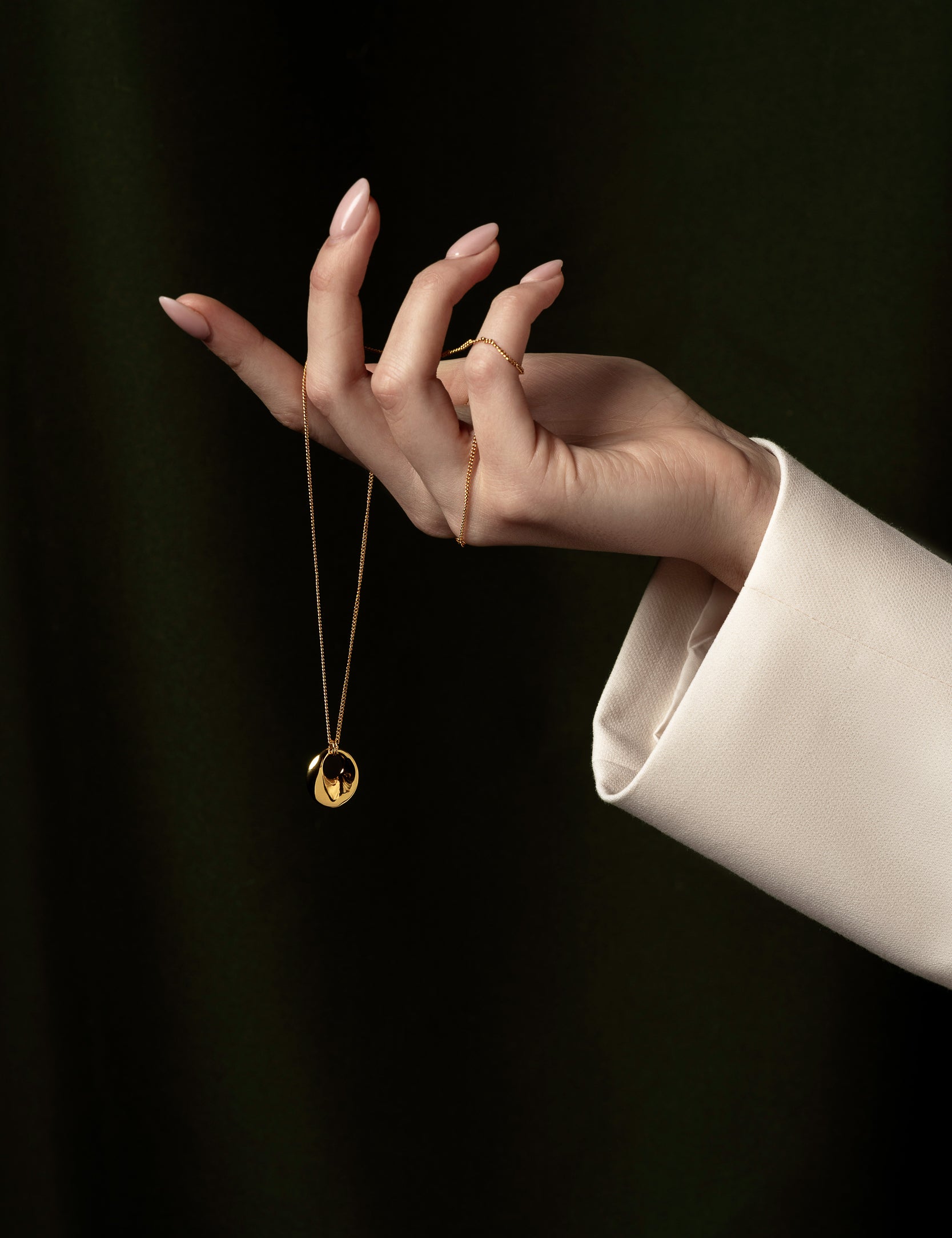 womans hand holding gold necklace around fingers and dropping the pendant 