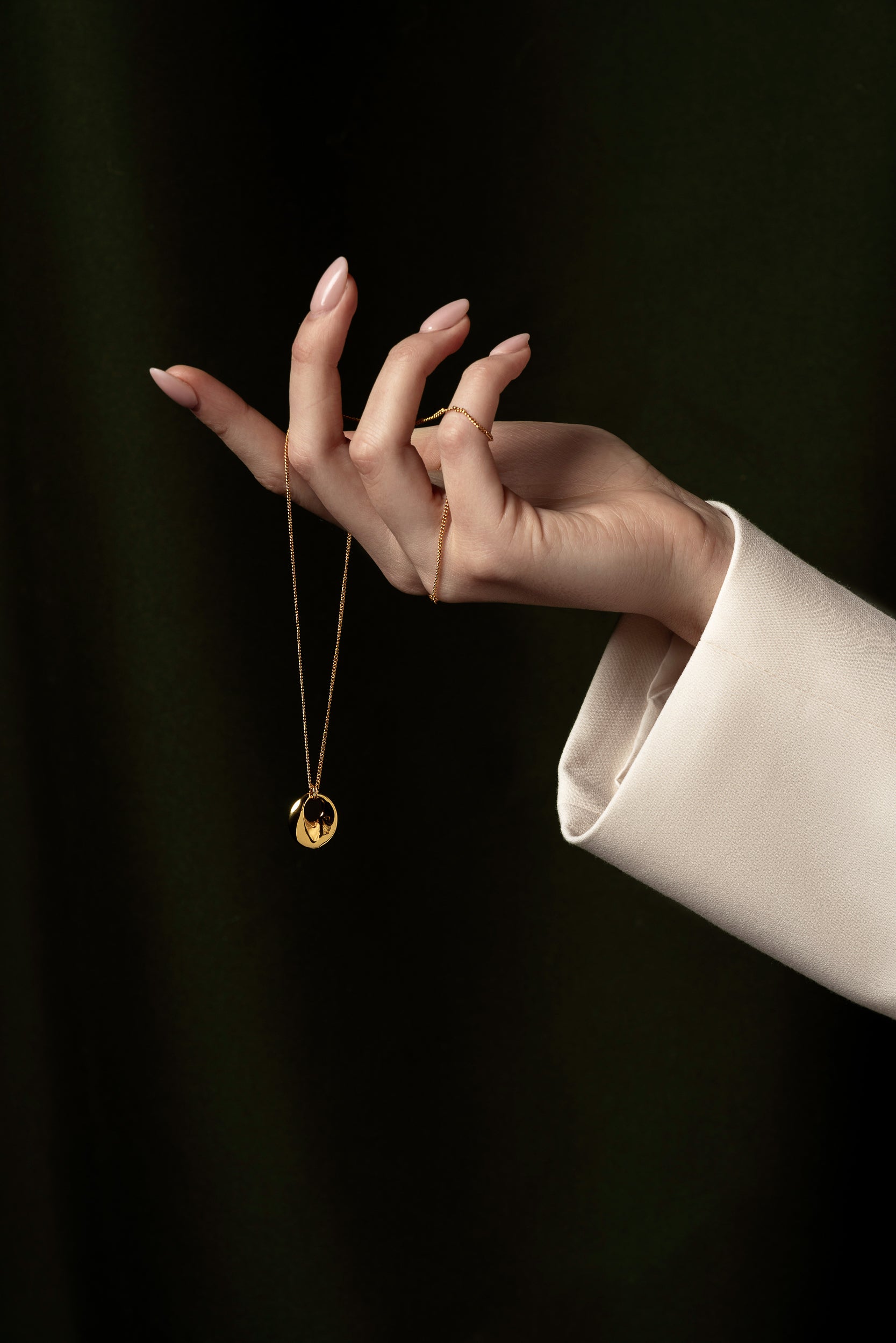 womans hand holding gold necklace around fingers and dropping the pendant 